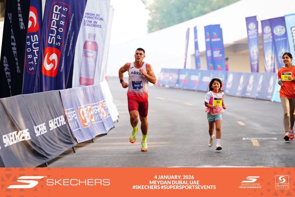 Adam Tuck crossing the finish alongside a young runner